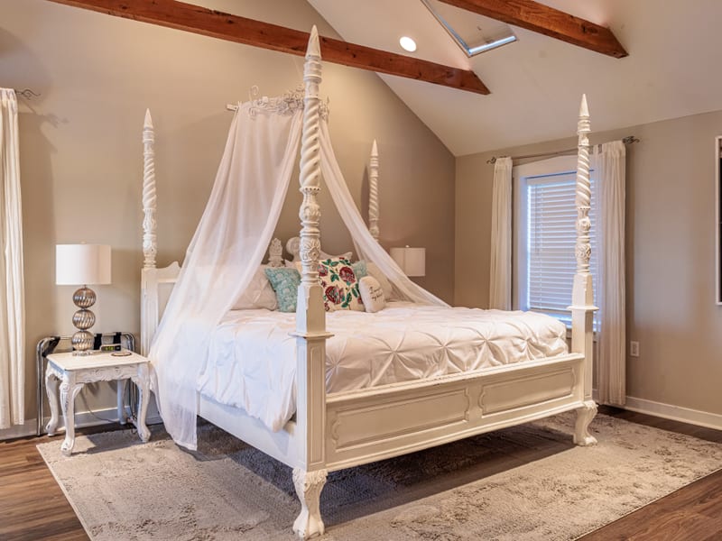 White four-poster king bed with sheer canopy under exposed wood beams in the cottage bedroom