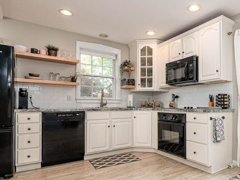 Cottage kitchen with white cabinets, subway-tile backsplash, open wood shelving, and a window above the sink
