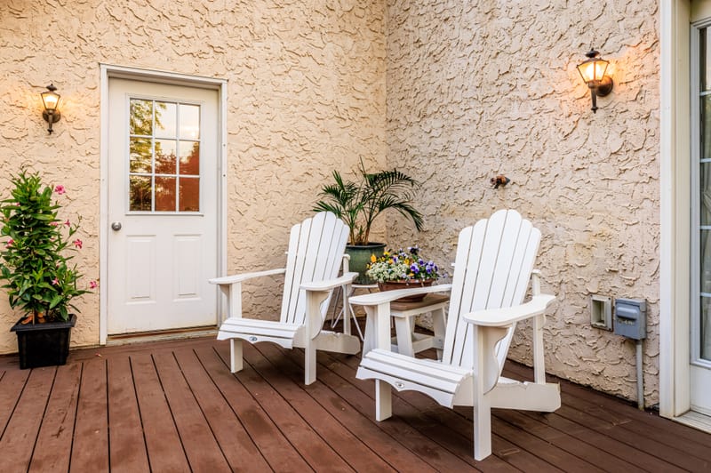 White Adirondack chairs on the cottage's back deck, with flower planters beside the door