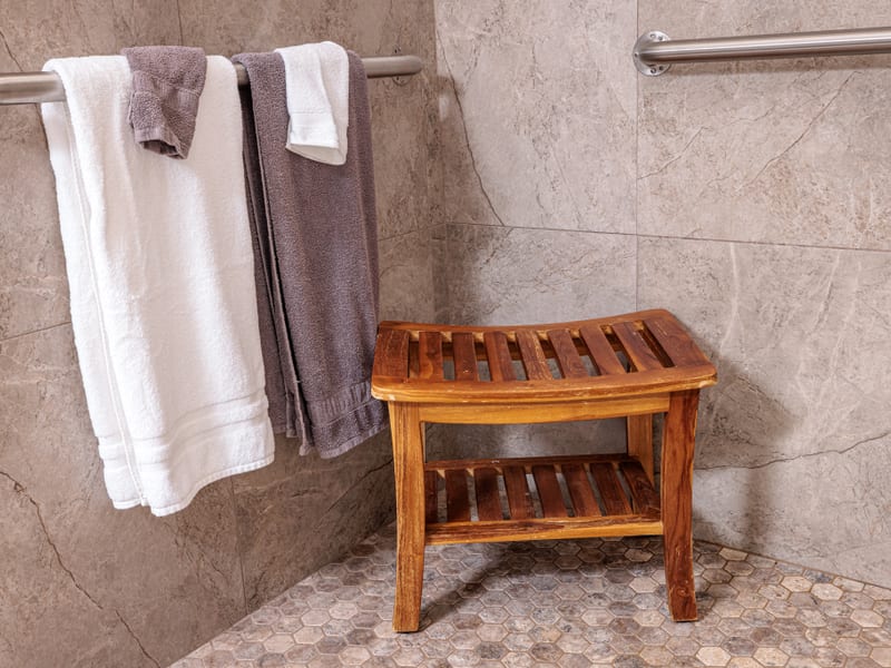 Spacious walk-in tile shower with a wooden teak bench and fresh towels on the rail