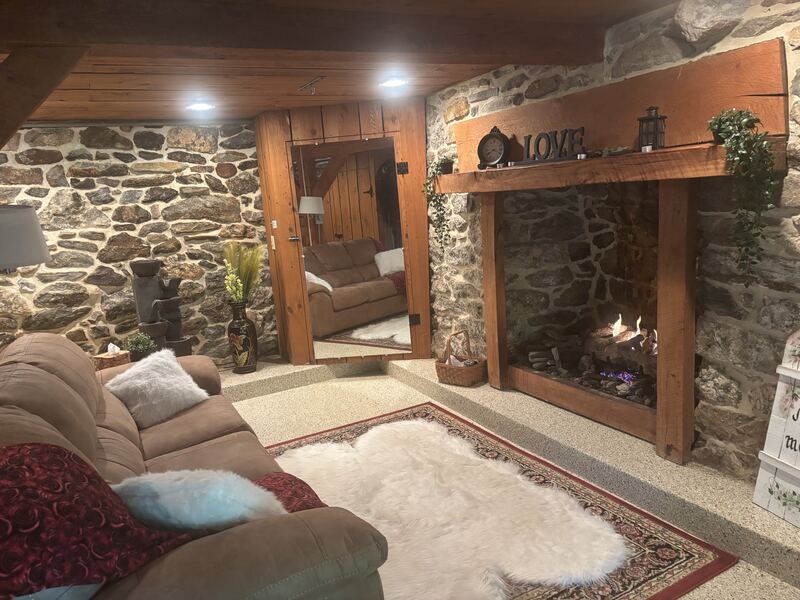 Cozy basement lounge with a plush sofa, stone walls, sheepskin rug, and wood-mantel fireplace