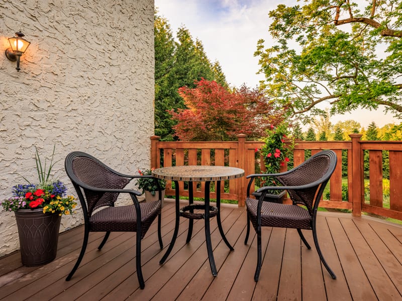 Wooden deck with a bistro table, wicker chairs, and blooming flowers at dusk