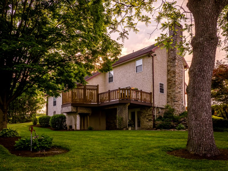 Back of the stone cottage with its raised wooden deck and stone chimney aglow at dusk