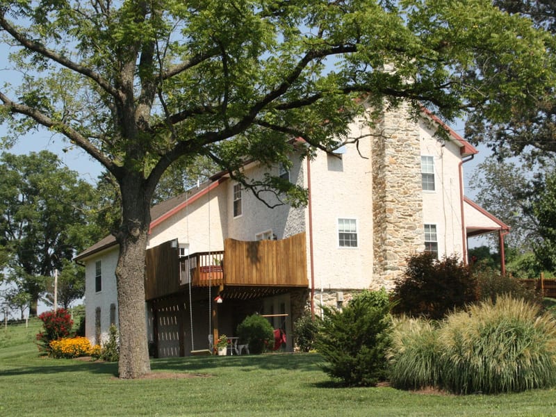 Stone cottage exterior with a wooden deck framed by mature shade trees