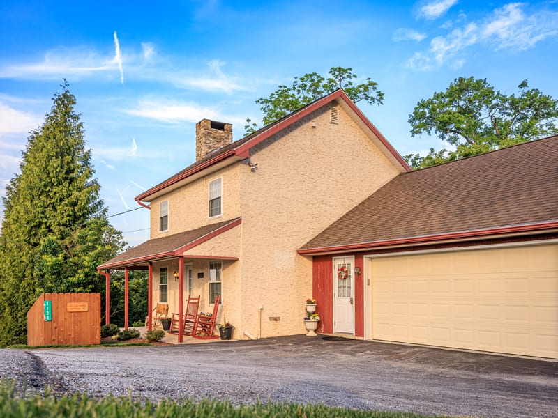 Stone cottage exterior with a covered porch and attached garage on a sunny day