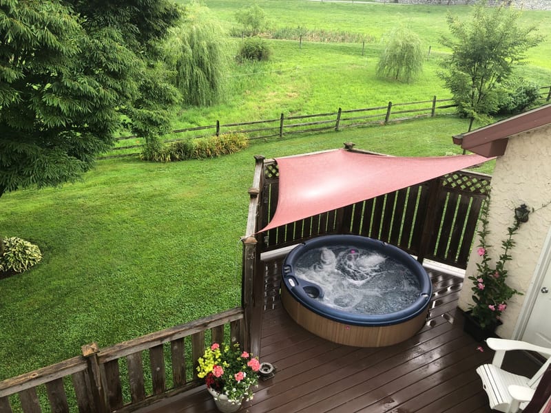 Bubbling hot tub shaded by a canopy on the deck, overlooking the green pasture