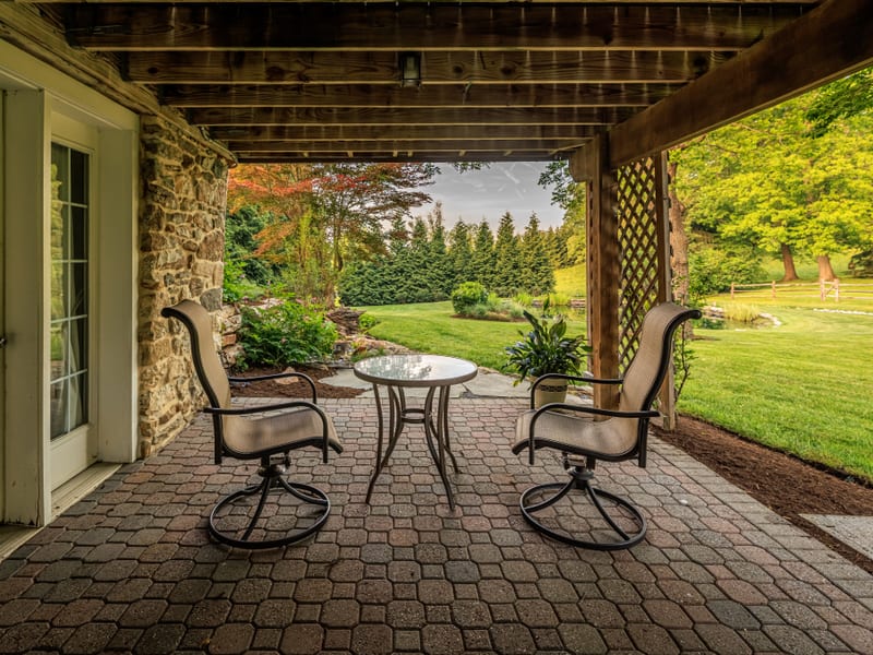 Covered stone patio with bistro seating overlooking the garden and rolling countryside