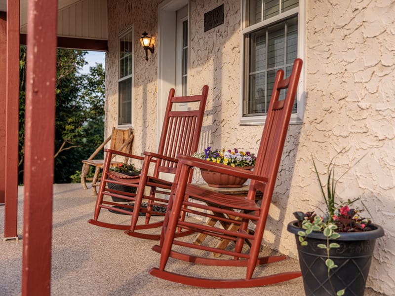 Two red rocking chairs on the covered front porch beside a pot of pansies