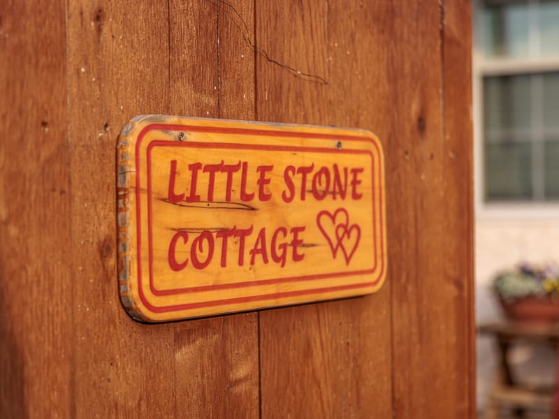 Hand-painted wooden 'Little Stone Cottage' sign with twin hearts hanging by the door